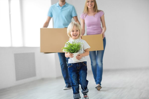 Child holding plant and adults holding boxes for new build home